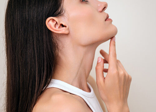 Profile view of woman with perfect face contour touching her neck.