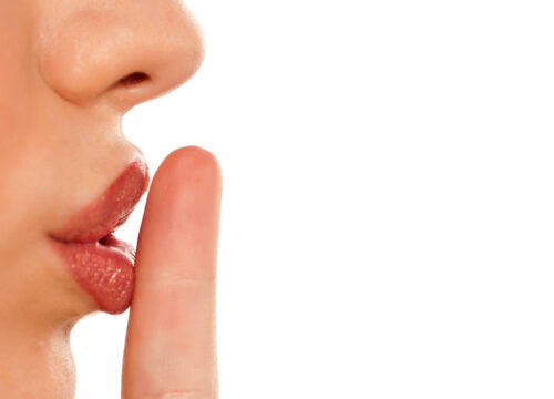 Photo of a woman putting her finger to her lips, making a silence gesture