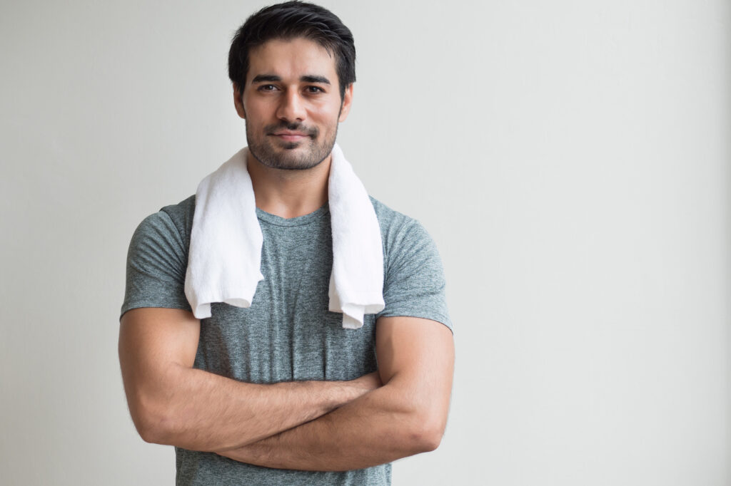 Photo of a man with a towel wrapped around his neck, wearing a gray shirt against a gray background