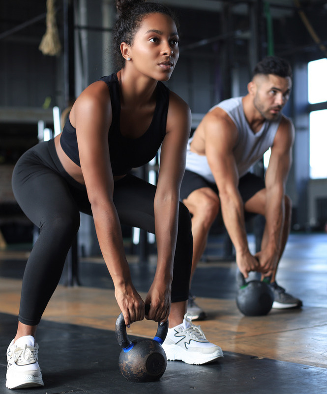 Photo of a woman and man working out with a kettle bell at the gym