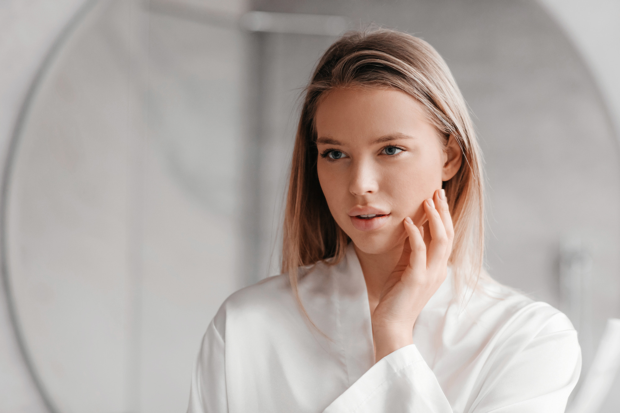 Attractive lady looking at her reflection in mirror and touching perfect skin, enjoying her appearance